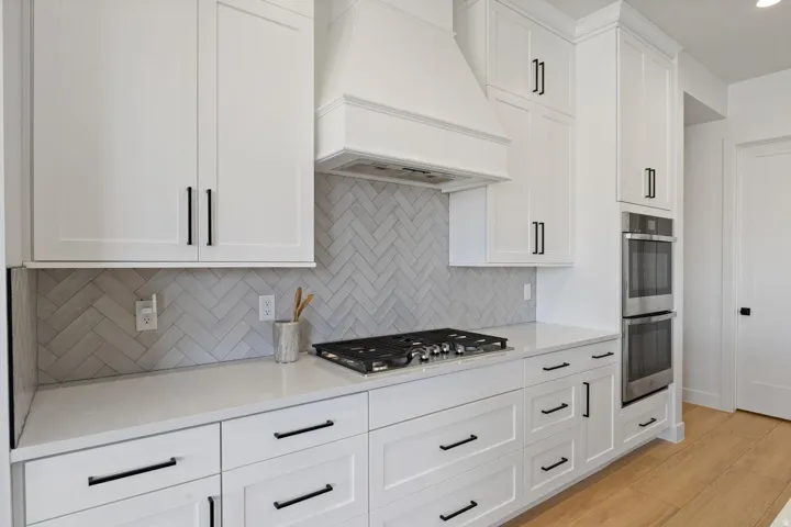 Chef's kitchen featuring white shaker cabinetry with black hardware, quartz countertops, and a herringbone tile backsplash
