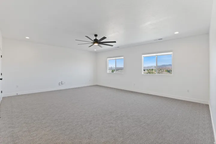 Spacious primary suite with carpeted flooring, ceiling fan with integrated lighting, and dual windows framing scenic mountain vistas