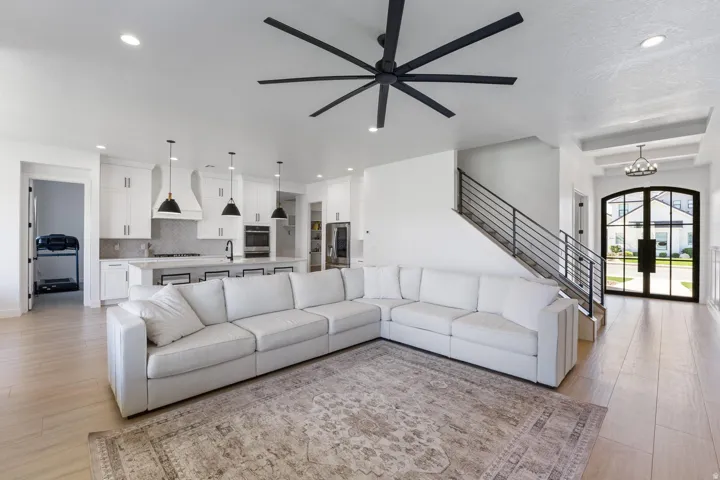 Open-concept living space featuring wood-finish flooring, a contemporary kitchen with white cabinetry and an island, a modern black ceiling fan, and a grand arched entry door with glass panels