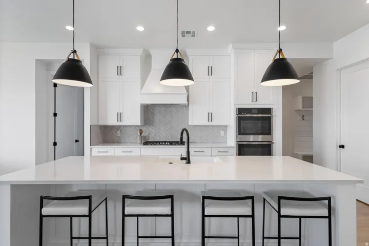 Contemporary kitchen featuring a white cabinetry and quartz countertop island with seating for four, stainless steel appliances including dual wall ovens and gas cooktop, pendant lighting with matte black shades and brass accents, and recessed ceiling lig