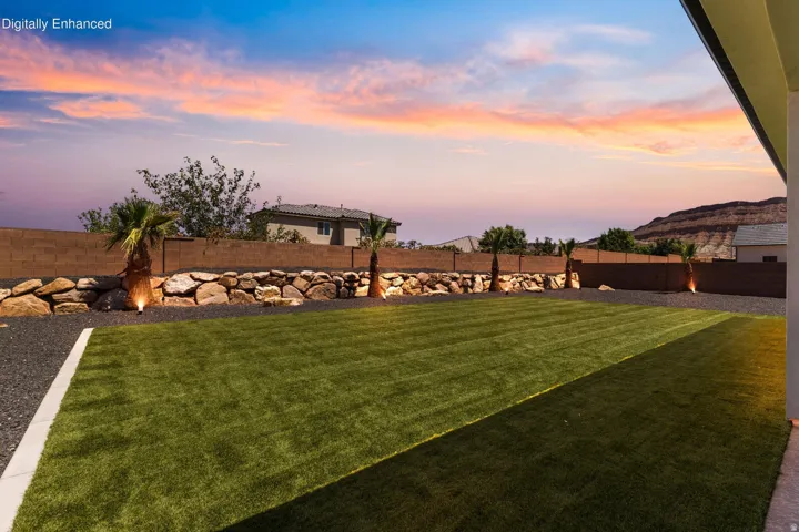 Expansive backyard featuring a manicured lawn, rock retaining wall, mature palm trees, and perimeter lighting