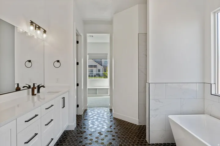 White double vanity with modern black hardware, black hexagonal floor tiles, freestanding soaking tub, and subway-tiled shower