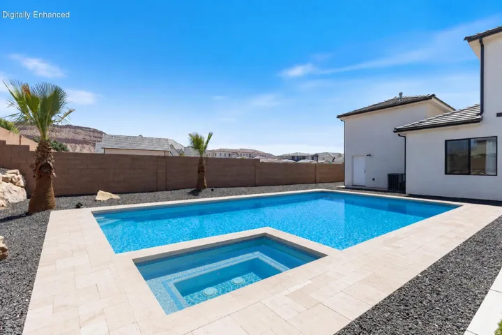 Outdoor swimming pool with integrated spa, bordered by light-toned paving and black rock landscaping
