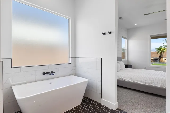Freestanding soaking tub with a wall-mounted matte black faucet, set against white tiled walls
