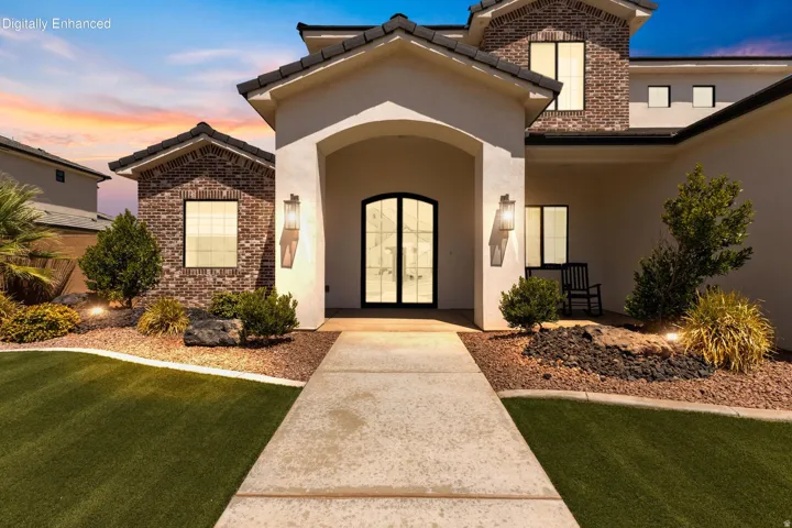 Stucco and brick facade with arched entryway, double pane front doors, and integrated outdoor lighting