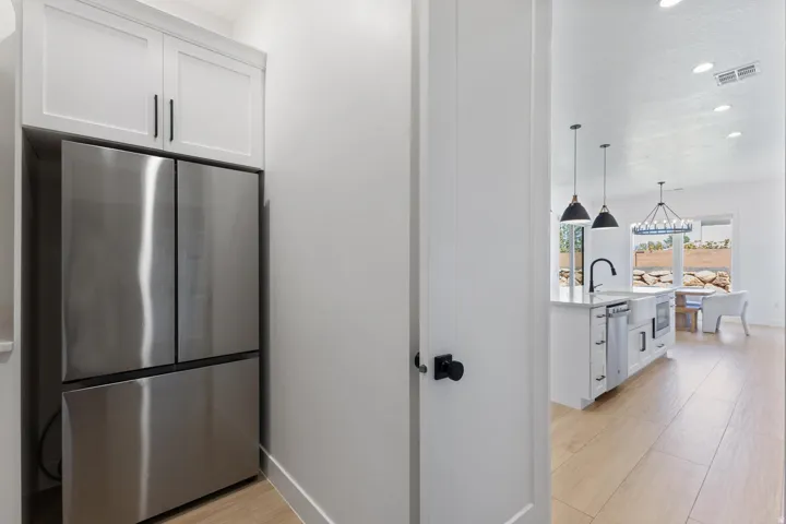 Modern kitchen featuring stainless steel French-door refrigerator with bottom freezer drawer, white cabinetry with hardware accents, wood-finish flooring, pendant lighting, and an open layout extending into the adjoining living space