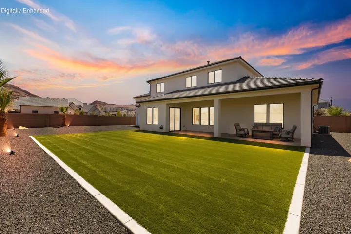 Stucco exterior with multiple windows, covered patio, artificial turf lawn, and gravel landscaping