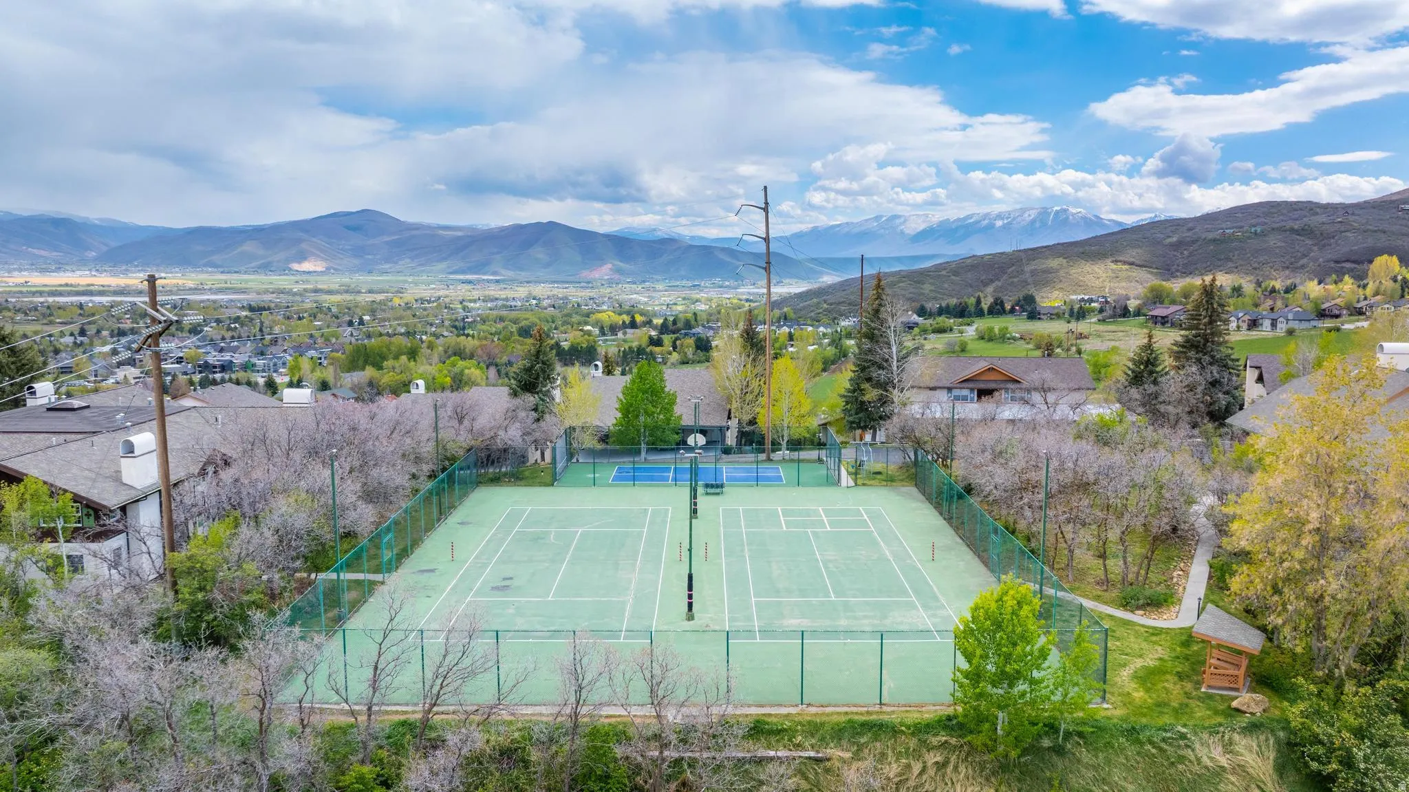 Tennis court with green surfacing, surrounded by a chain-link fence, situated on a hillside