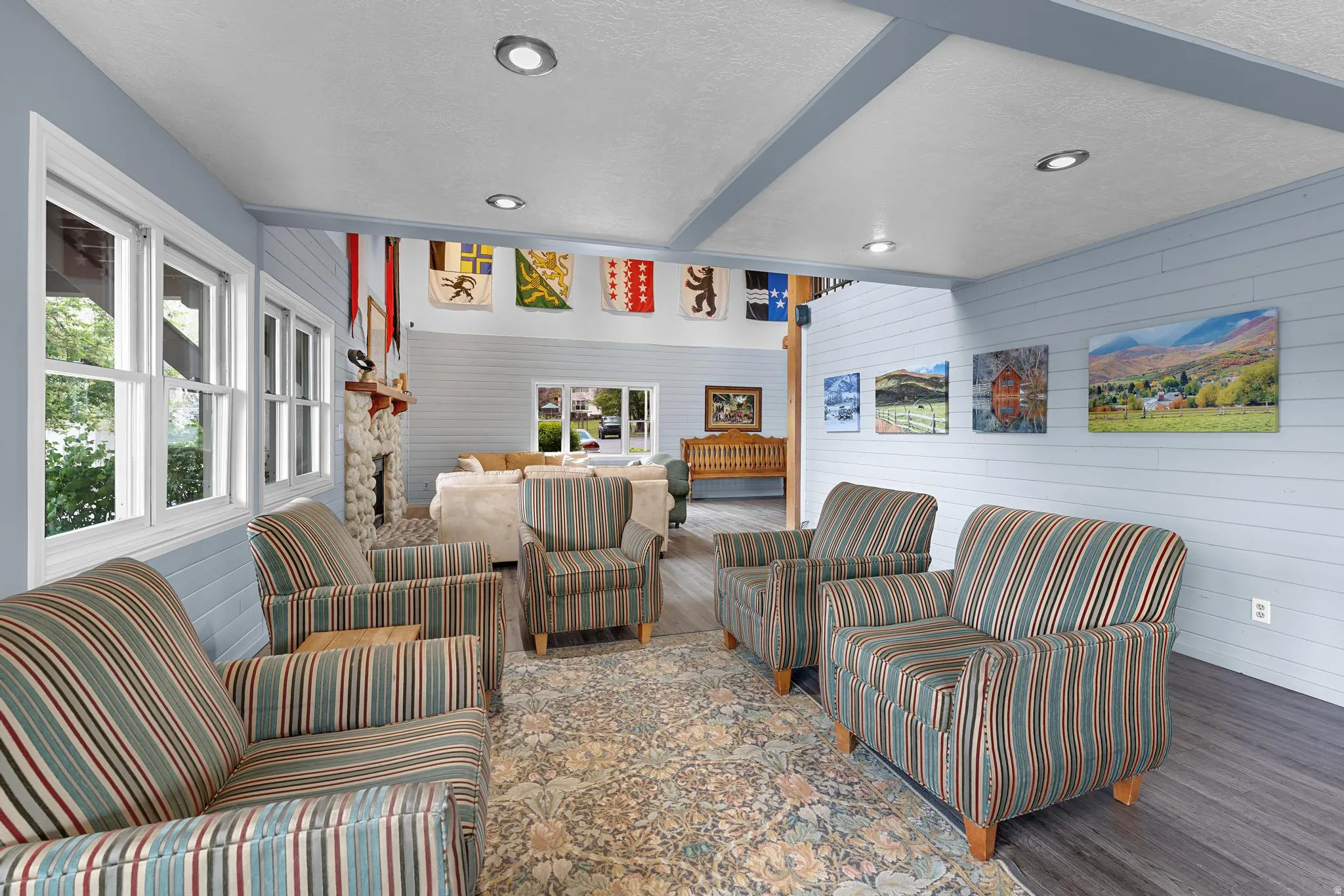 Spacious common area featuring shiplap walls, recessed lighting, wood-finish flooring, multiple windows, and a stone fireplace