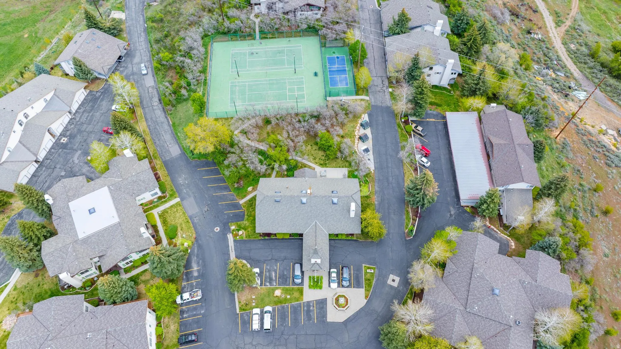Community tennis courts, paved parking areas, multiple residential structures, and mature trees