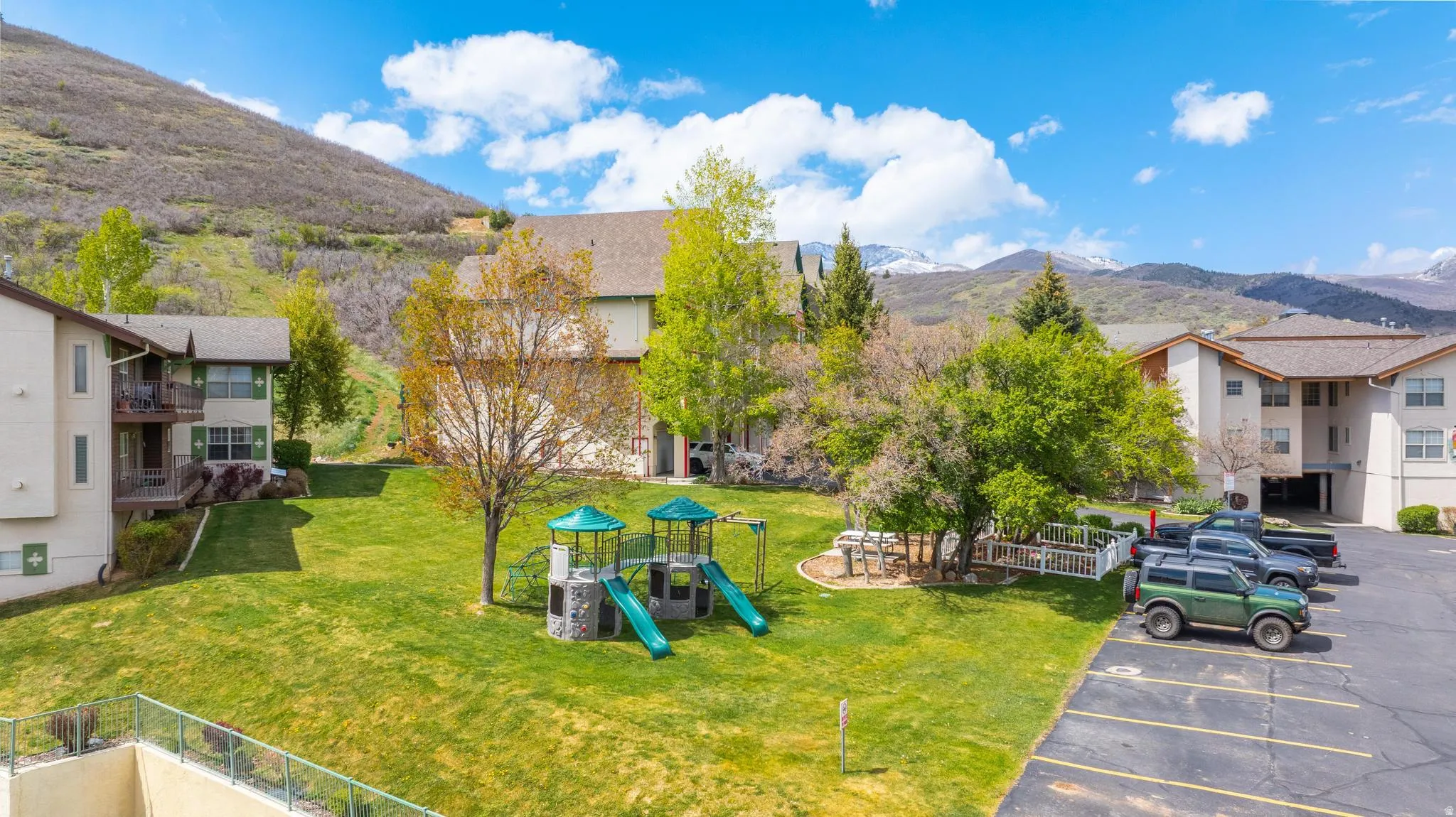 Expansive green space with a playground, multiple residential buildings with balconies, and dedicated parking