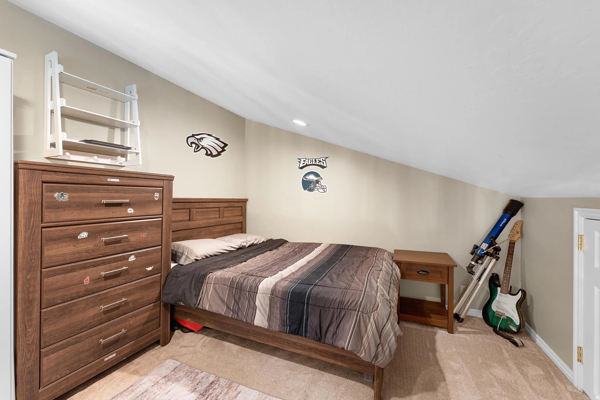 Recessed lighting illuminates the carpeted flooring and sloped ceiling