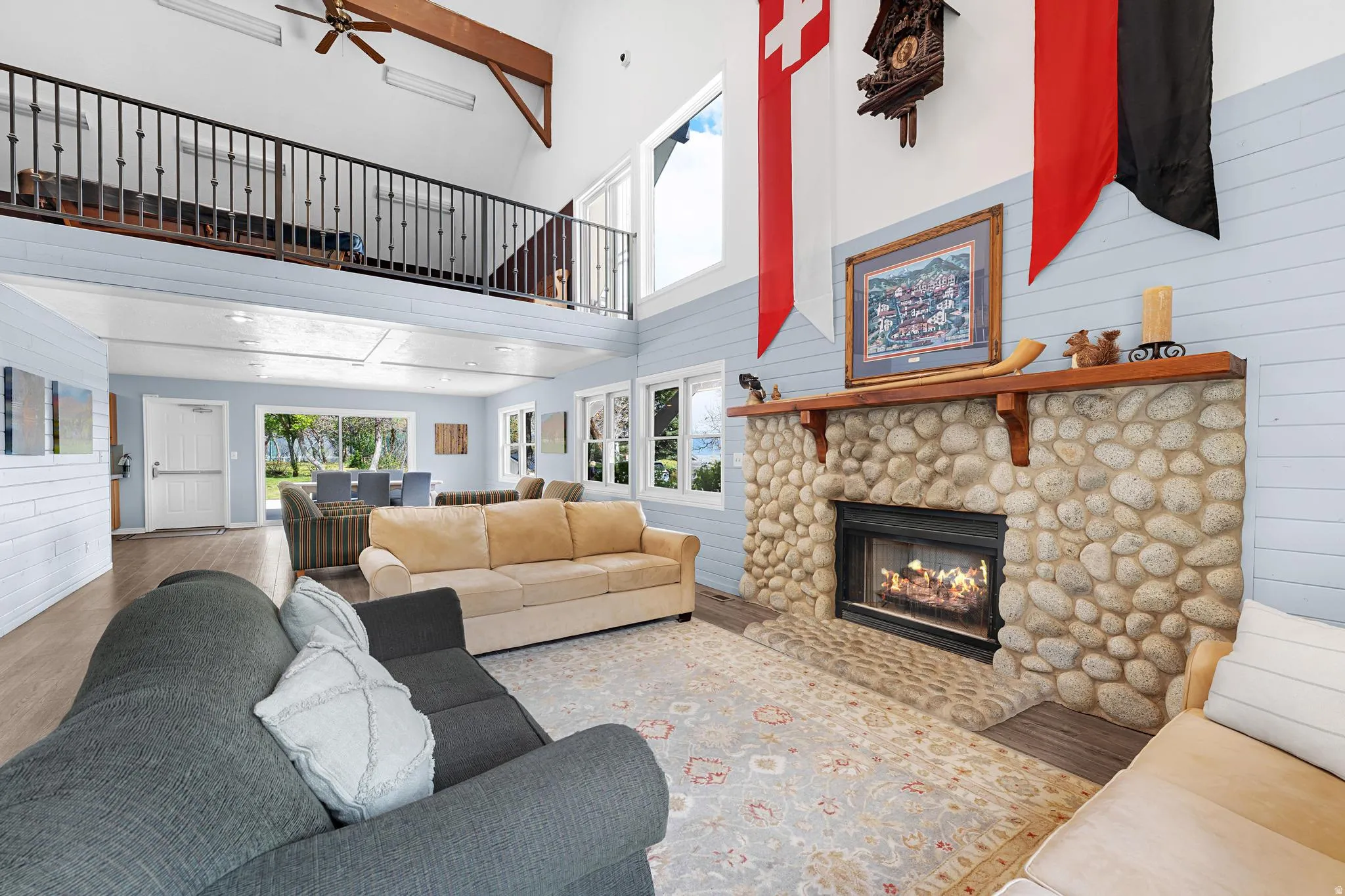 Vaulted ceilings with exposed wood beams, a stone-clad fireplace with a wood mantel, and large windows