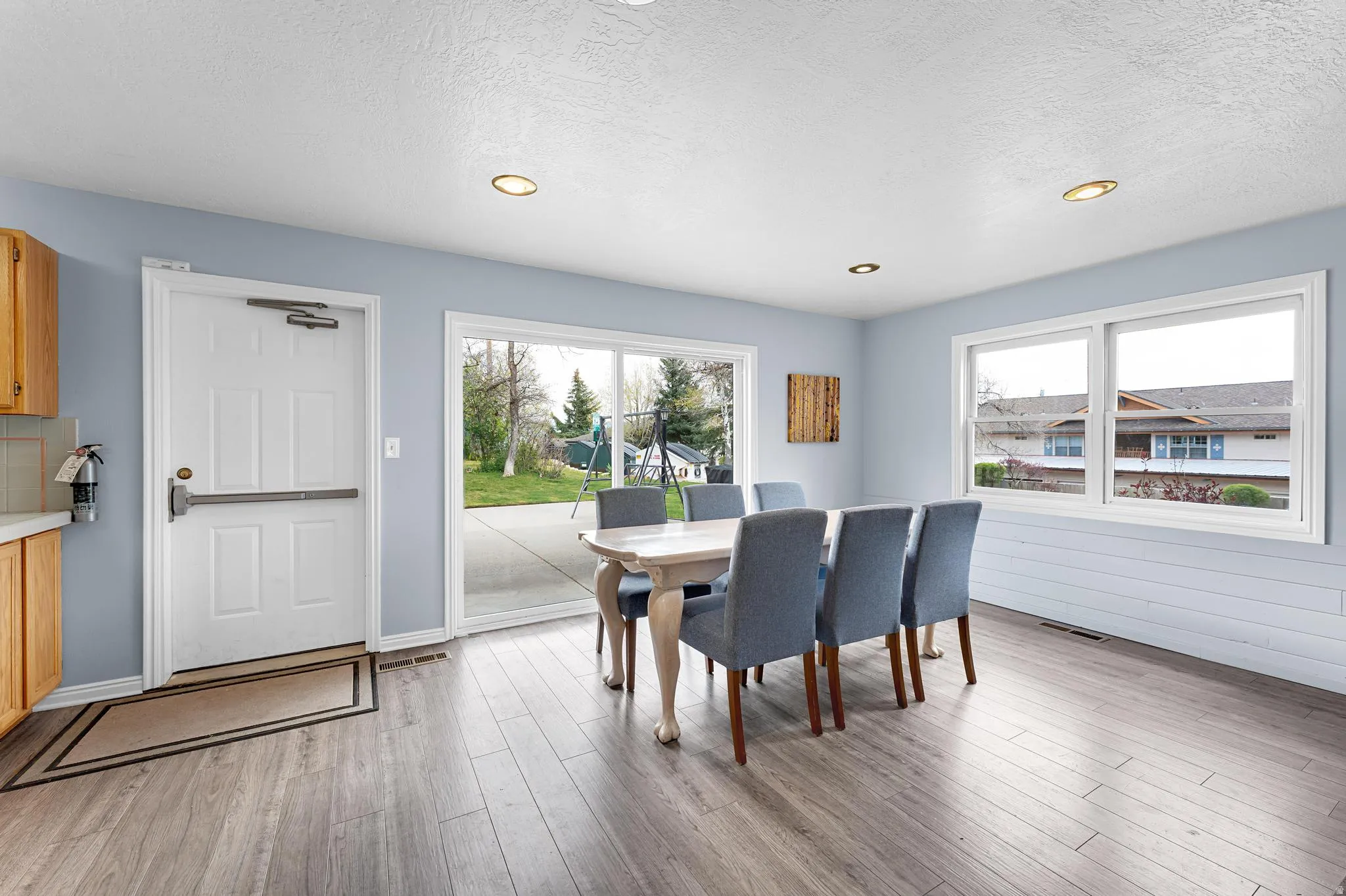 Wood-finish flooring, recessed ceiling lighting, light blue wall paint, white trim windows, and a sliding glass door