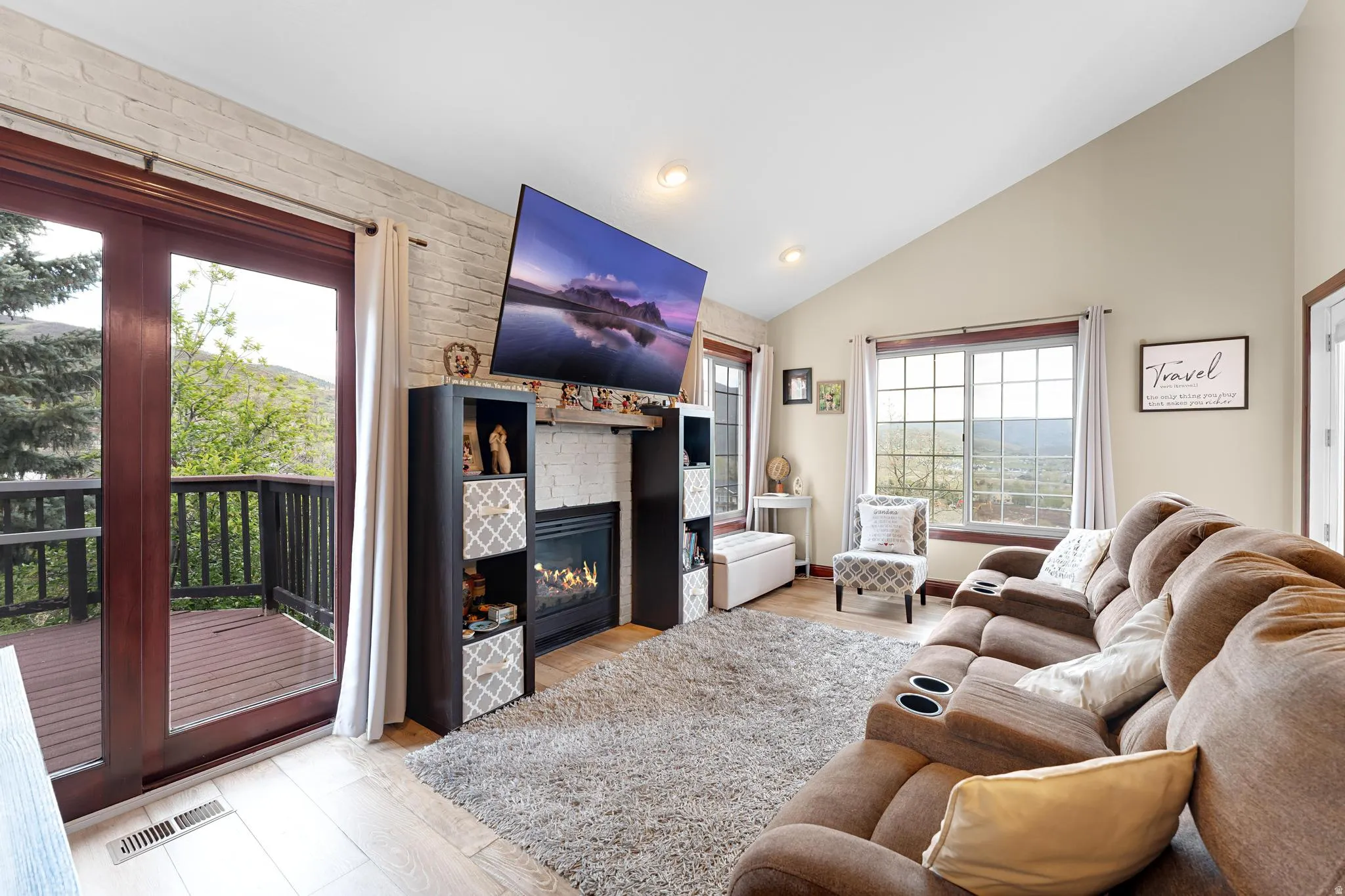 Vaulted ceiling, stone accent wall with built-in fireplace, wood-finish flooring, multiple windows, and exterior balcony access