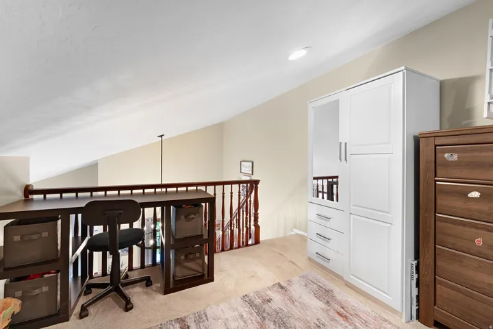Carpeted loft area with sloped ceilings, recessed lighting, and a wood-finish railing