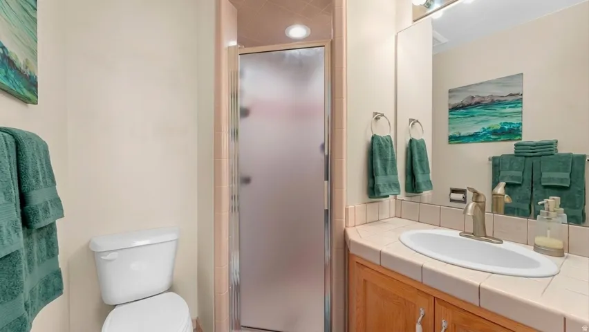 Frosted glass shower enclosure, vanity with integrated sink, tile countertop, wood-finish cabinetry, and overhead vanity lighting