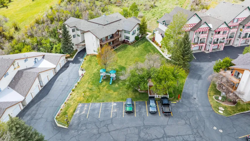 Multiple residential structures with pitched roofs, a paved parking area, and mature trees