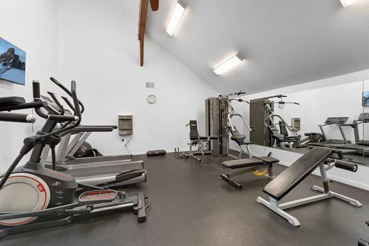 Fitness area with vaulted ceilings, exposed wood beams, wall-mounted television, full-wall mirror, and durable rubber flooring