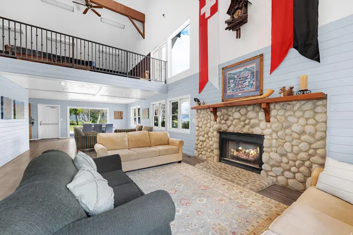 Vaulted ceilings with exposed wood beams, a stone-clad fireplace with a wood mantel, and large windows