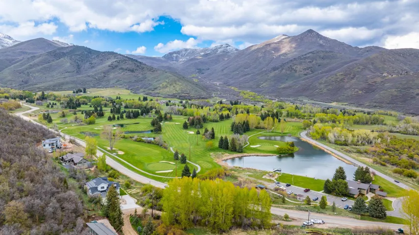 Mountainous landscape with a golf course, expansive pond, and lush green fairways