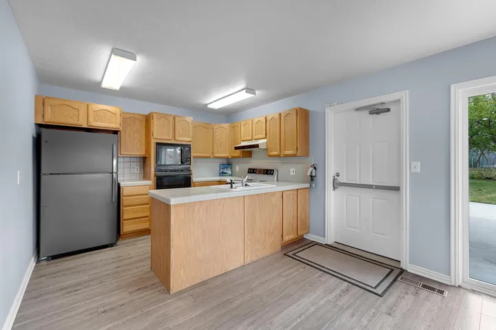 Kitchen featuring wood-finish cabinetry, a central island, light-toned countertops, and wood-finish flooring