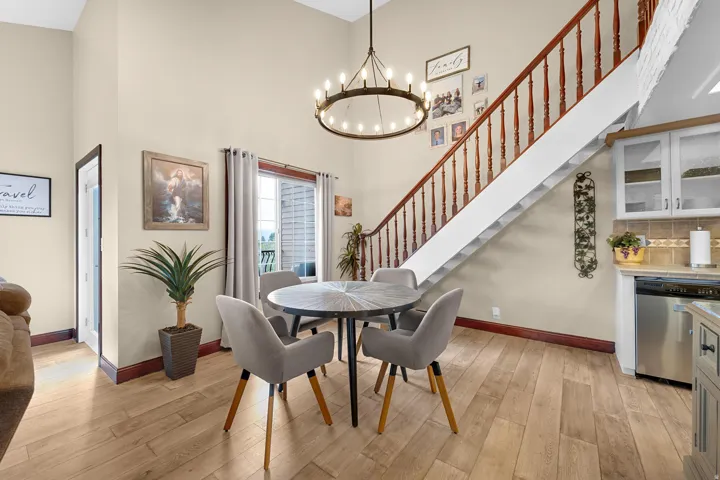 Vaulted ceiling with a large chandelier, wood-finish flooring, staircase with wood banister, and sliding glass door