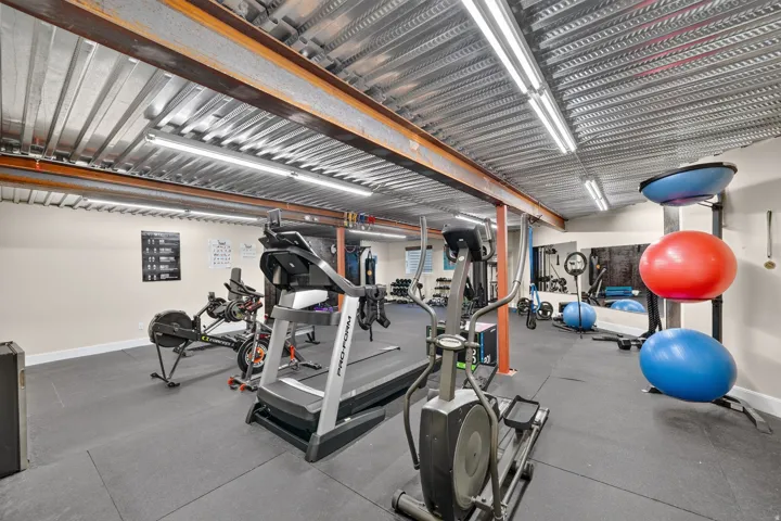 Dedicated fitness area featuring rubber flooring, exposed metal ceiling, recessed linear lighting, and a mirrored wall