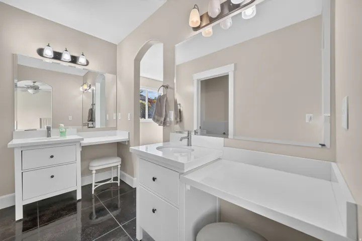Dual vanity with integrated sinks, expansive counter space, dark tile flooring, and arched entryway