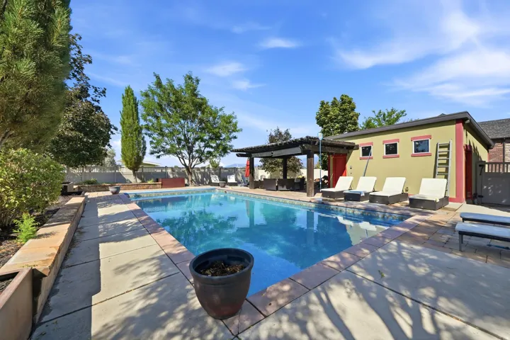 Outdoor swimming pool with a mosaic tile interior, surrounding concrete patio, and a pergola structure