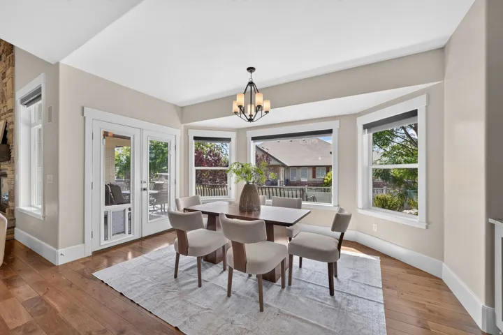 Hardwood flooring, bay window with multiple panes, stone wall accent, double glass-paneled doors, and a built-in chandelier