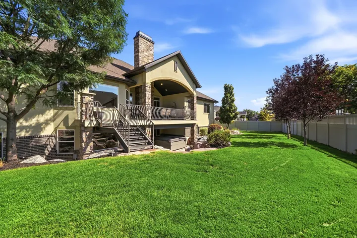 Expansive manicured lawn with mature trees, a covered patio, and an exterior hot tub
