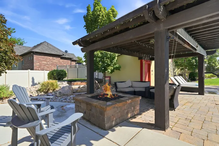 Expansive patio featuring a stone-finish fire pit, a dark wood pergola, and paver flooring
