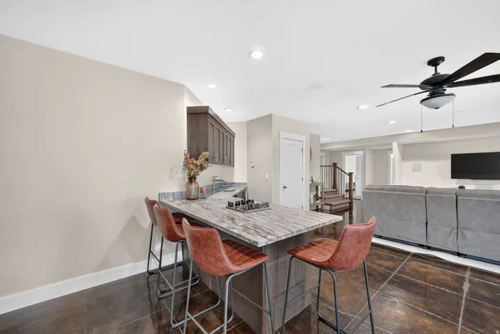 Kitchenette with stone countertop, dark wood-finish cabinetry, stainless steel sink, and dark tile flooring