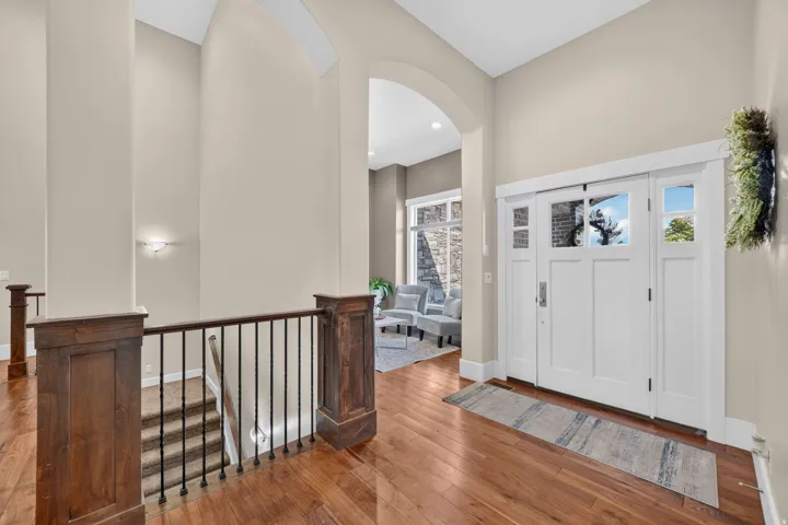 Entryway with wood-finish flooring, a white paneled door with sidelights, and a staircase featuring dark wood newel posts and wrought iron balusters