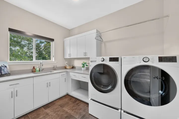 Spacious utility room featuring white cabinetry, light-toned countertops, a utility sink with a high-arch faucet, a window, and wood-finish flooring