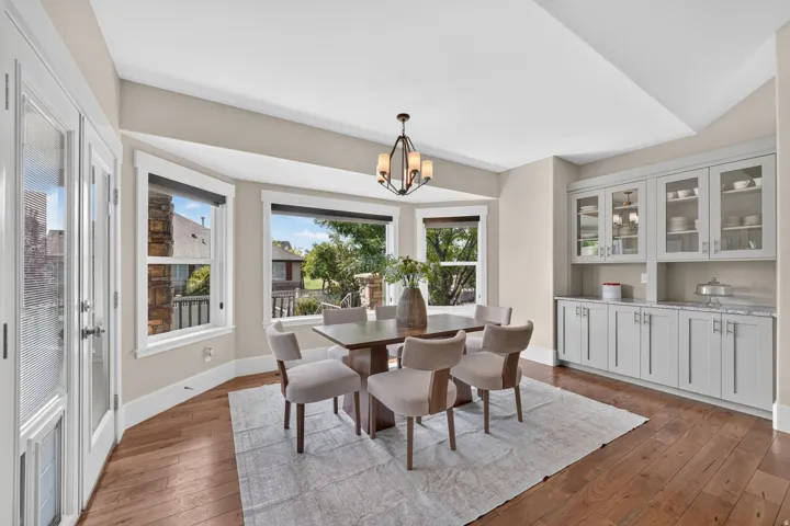 Hardwood flooring, built-in cabinetry with glass-front uppers, bay windows, and a chandelier