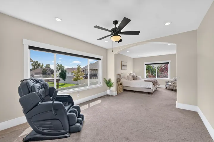 Recessed lighting, large windows with white trim, soft gray carpeting, and a ceiling fan with light fixture