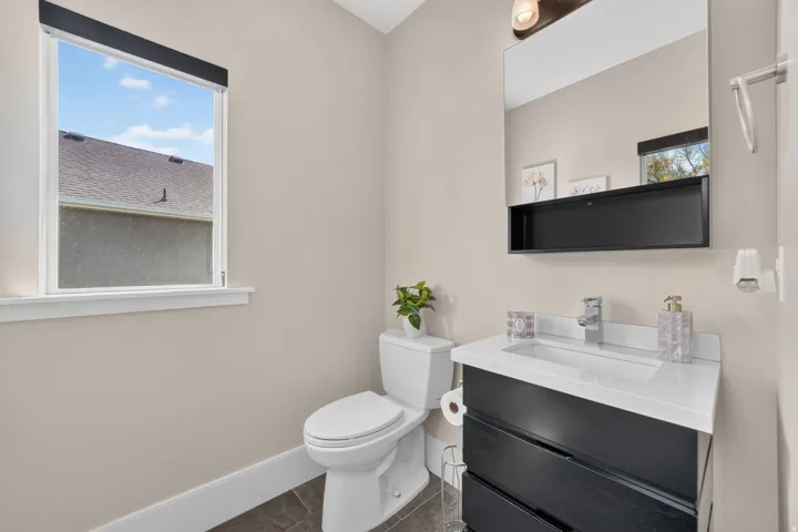 Black vanity with an integrated white rectangular sink, framed mirror, and a wall-mounted light fixture