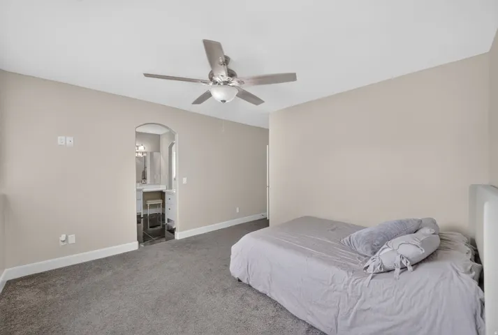 Carpeted flooring, ceiling fan with integrated lighting, neutral wall paint, arched doorway, and white trim