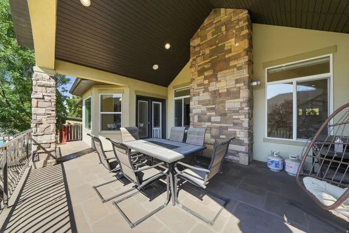 Covered outdoor patio with a stone-clad column and fireplace, transom windows, and a black wrought iron railing