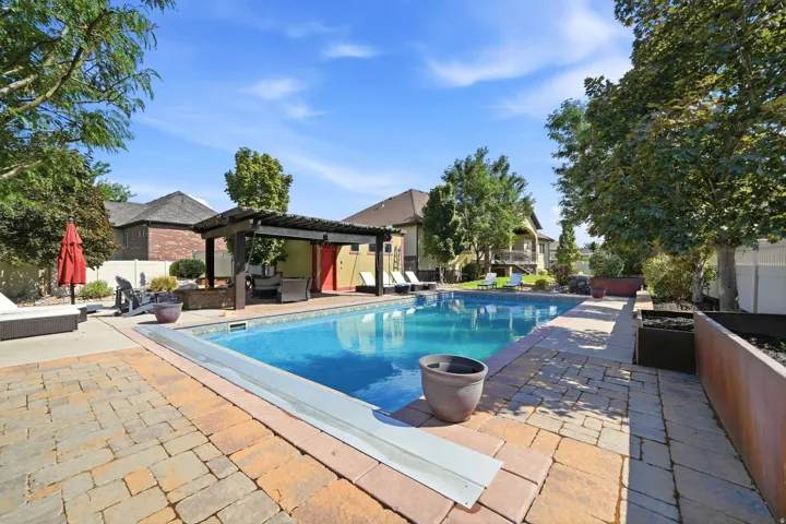 Outdoor swimming pool surrounded by paver patio, featuring a shaded pergola structure, and landscaping