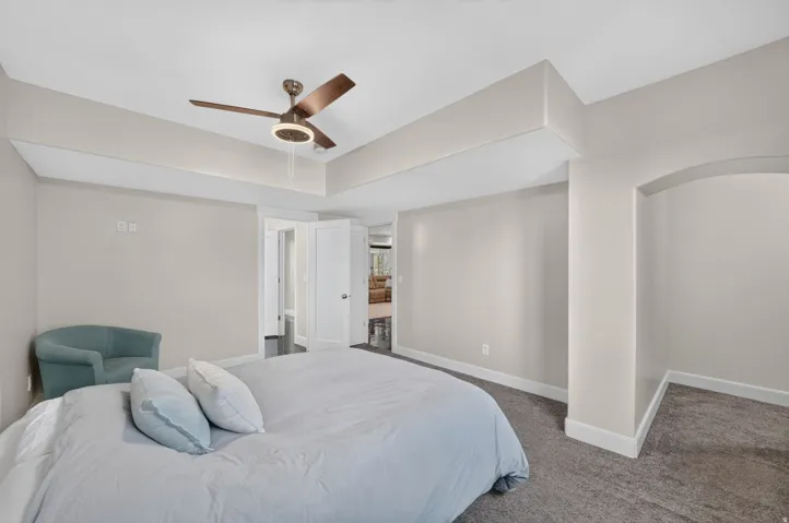 Tray ceiling with a ceiling fan, neutral wall tones, arched alcove, and soft carpet flooring