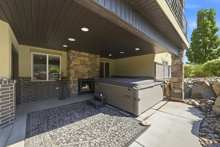 Covered patio featuring recessed lighting, a built-in fireplace, a hot tub, and stone accent pillars
