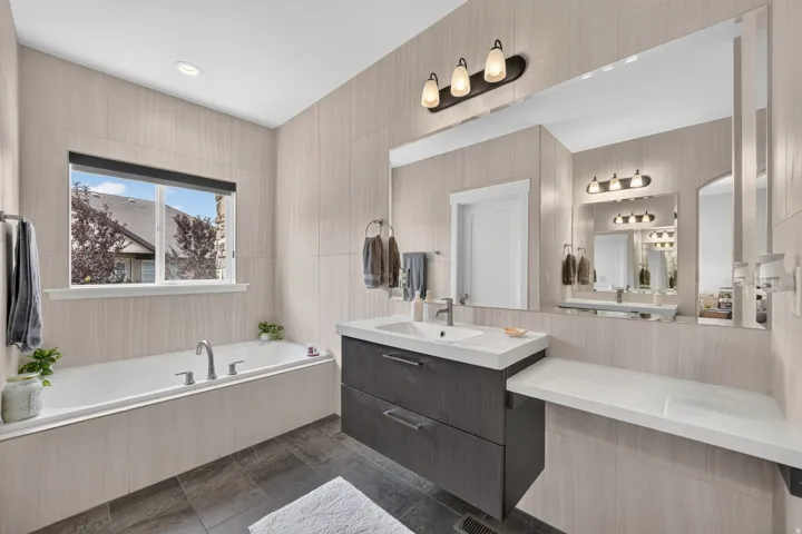 Soaking tub with a wall-mounted faucet, dark wood-finish vanity with a single basin, and expansive wall-to-wall mirror