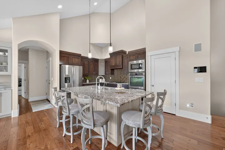 Kitchen featuring vaulted ceilings, wood-finish flooring, a central island with a stone countertop, built-in stainless steel appliances, and dark wood cabinetry