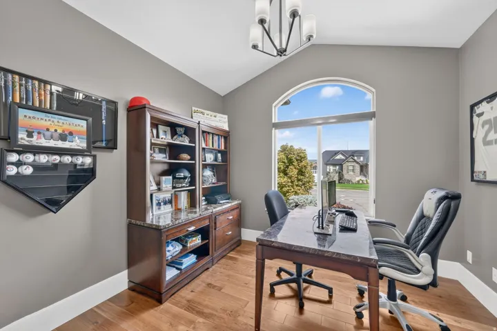 Vaulted ceiling with a contemporary chandelier, arched top window, wood-finish flooring, and built-in cabinetry with a stone countertop