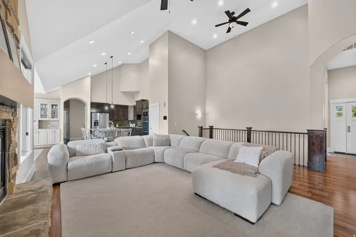Vaulted ceilings with recessed lighting, wood-finish flooring, a stone fireplace, and a wrought iron balcony railing