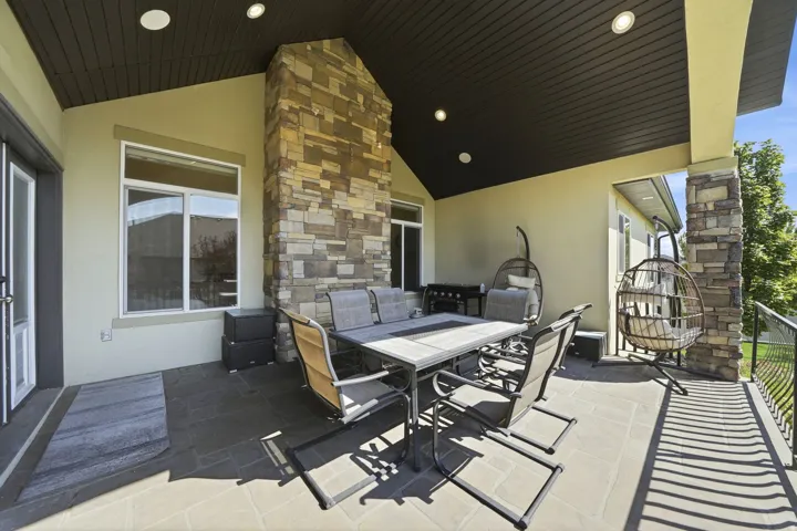 Expansive covered patio featuring a stone-clad pillar, stone-clad fireplace, recessed lighting, and a metal railing