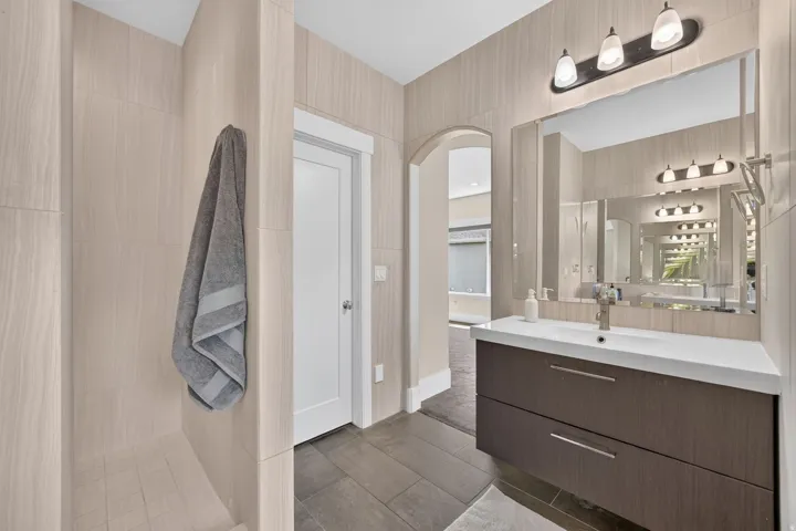 Walk-in shower with light-toned tiled walls, floating vanity with dual drawers, integrated sink, and an arched doorway